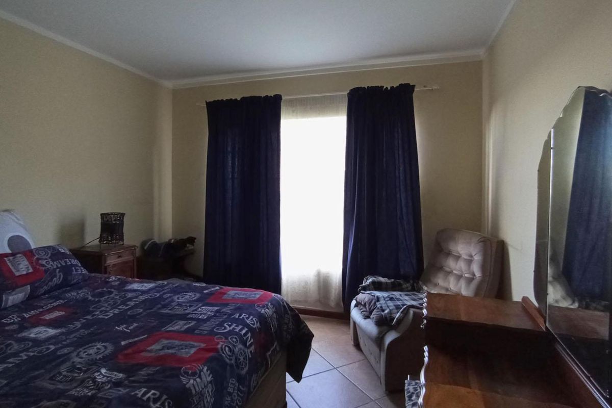 A standard bedroom featuring tiled flooring and a window with dark curtains, providing a functional and lived-in space.