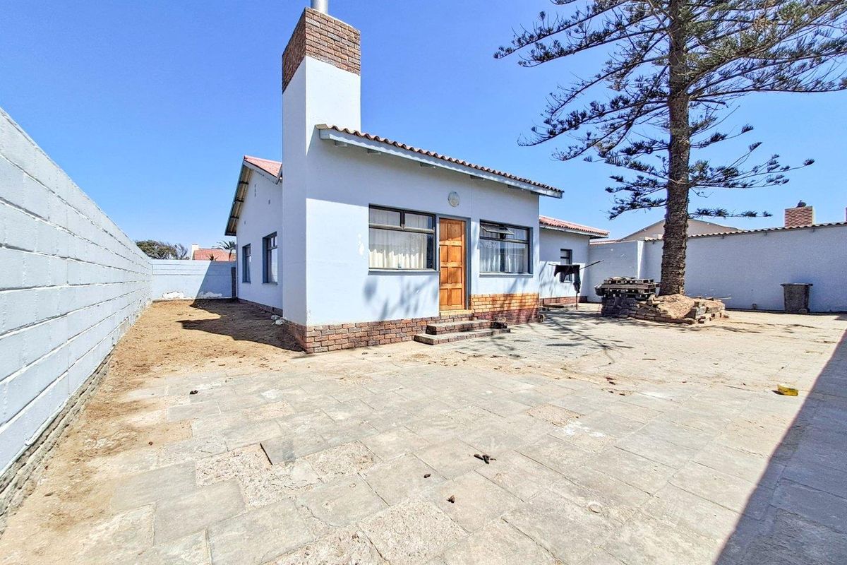 Rear exterior view of the house featuring a brick chimney, paved courtyard area, and perimeter boundary walls.