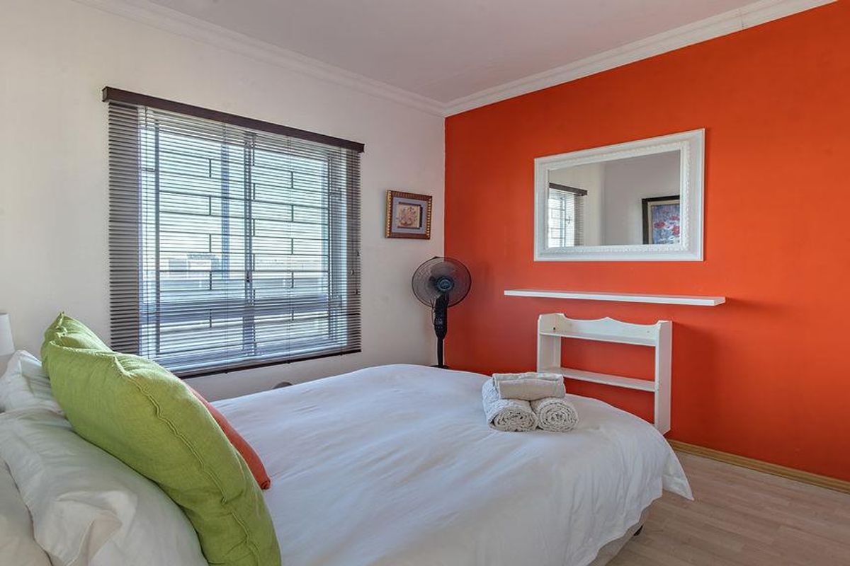 A bedroom featuring laminate flooring, a window with security bars, and a bold orange accent wall.