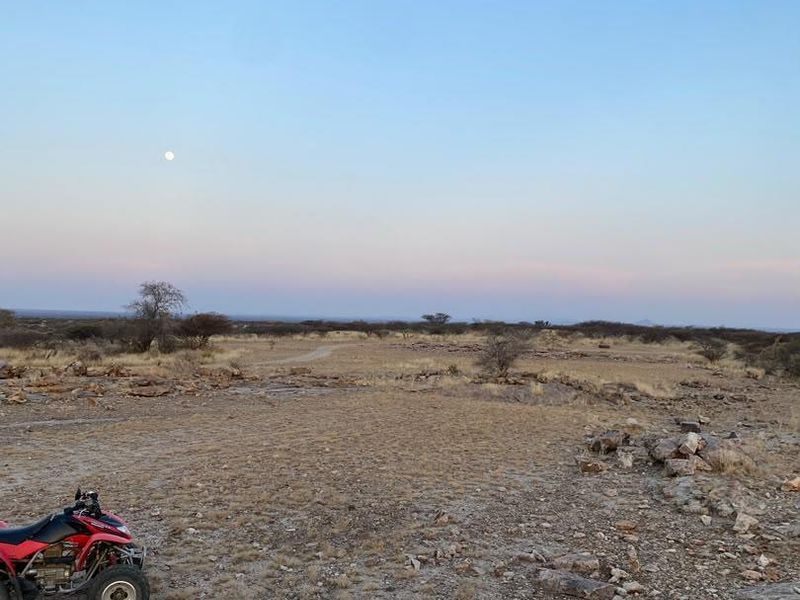 A wide-angle view of the expansive, arid farm landscape at dusk, featuring natural rocky terrain and open veld.