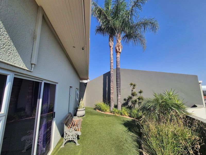 A private rear garden area featuring artificial turf, mature palm trees, and direct access to the interior via sliding glass doors.