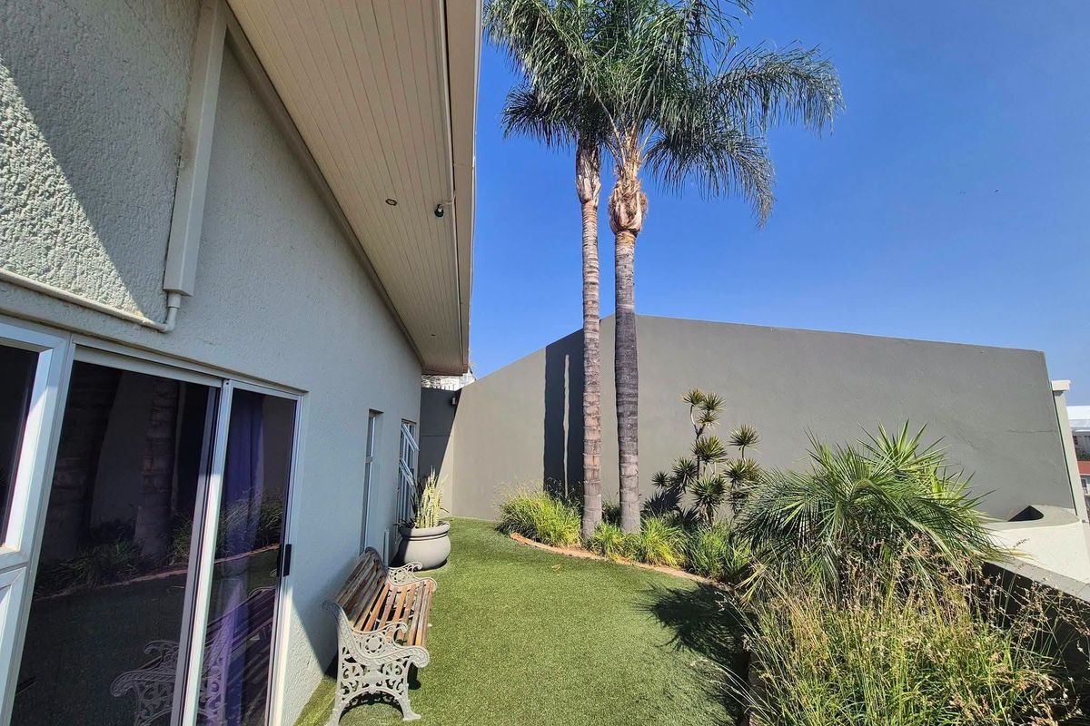A private rear garden area featuring artificial turf, mature palm trees, and direct access to the interior via sliding glass doors.
