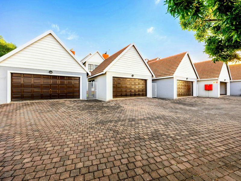 A row of well-maintained residential garages featuring brown sectional doors, tiled gable roofs, and a paved driveway area.