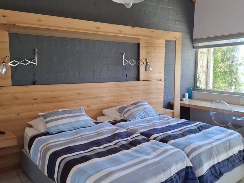 A well-maintained bedroom featuring exposed timber rafters, a custom built-in timber headboard, a dedicated desk area, and modern tiled flooring.