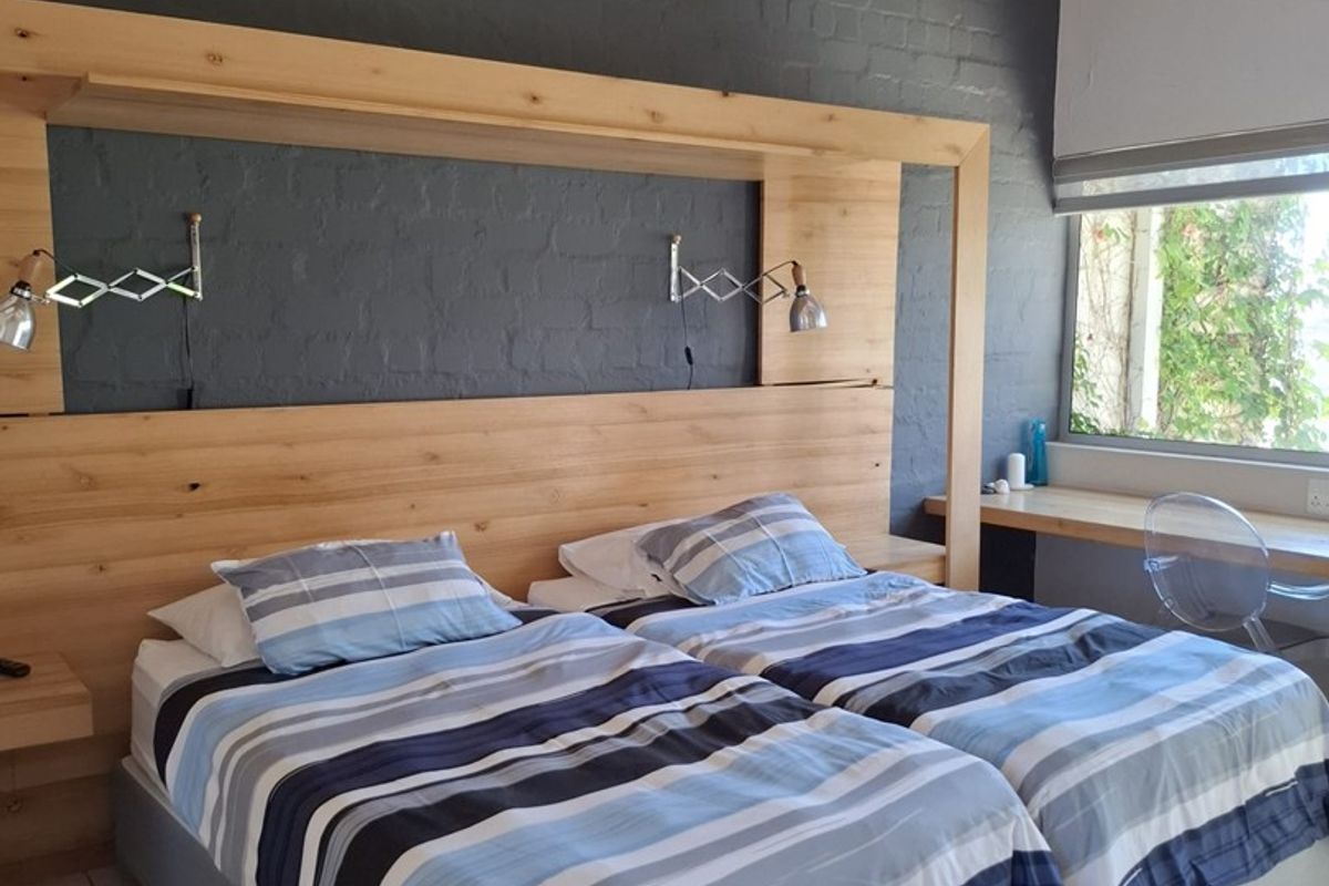 A well-maintained bedroom featuring exposed timber rafters, a custom built-in timber headboard, a dedicated desk area, and modern tiled flooring.