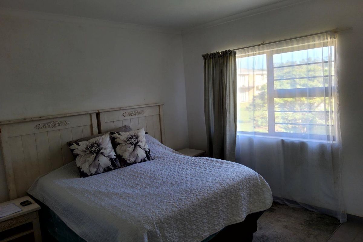 A bedroom featuring a large window with natural light, neutral wall finishes, and tiled flooring.