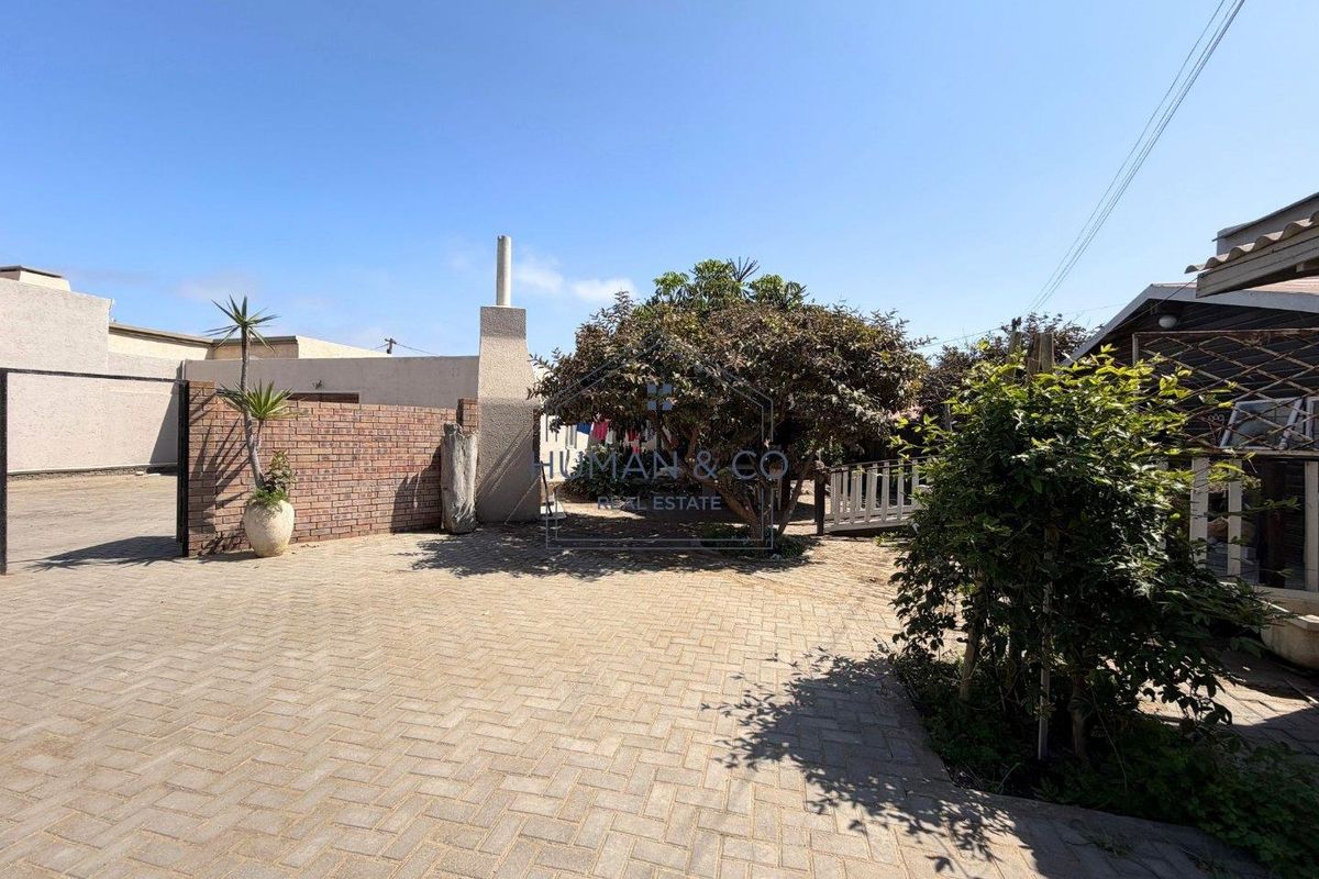 A paved rear courtyard area featuring a brick boundary wall, an outdoor fireplace, and established garden greenery.