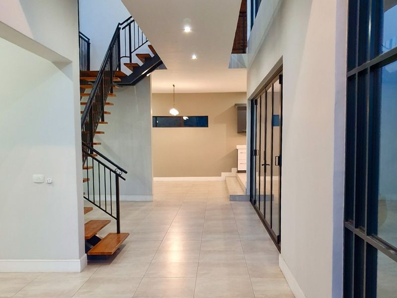 Spacious modern hallway featuring a striking open-tread staircase with metal balustrades, large format floor tiles, and expansive glass doors leading to adjacent living areas.