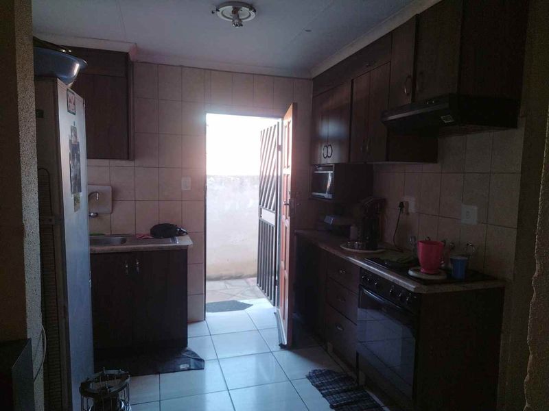 A functional kitchen featuring dark built-in cabinetry, tiled splashbacks, and direct access to an outdoor area through a security gate.