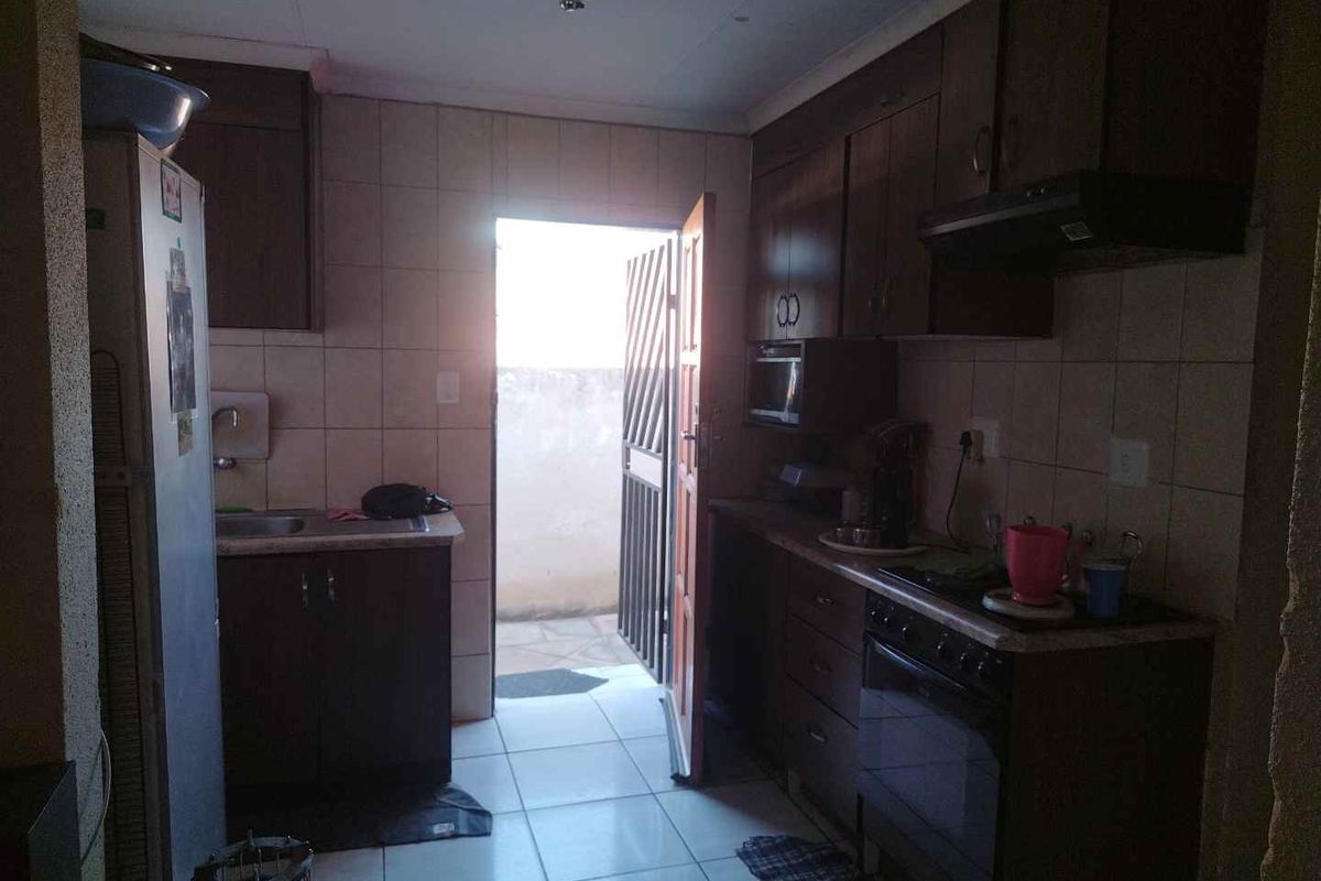 A functional kitchen featuring dark built-in cabinetry, tiled splashbacks, and direct access to an outdoor area through a security gate.
