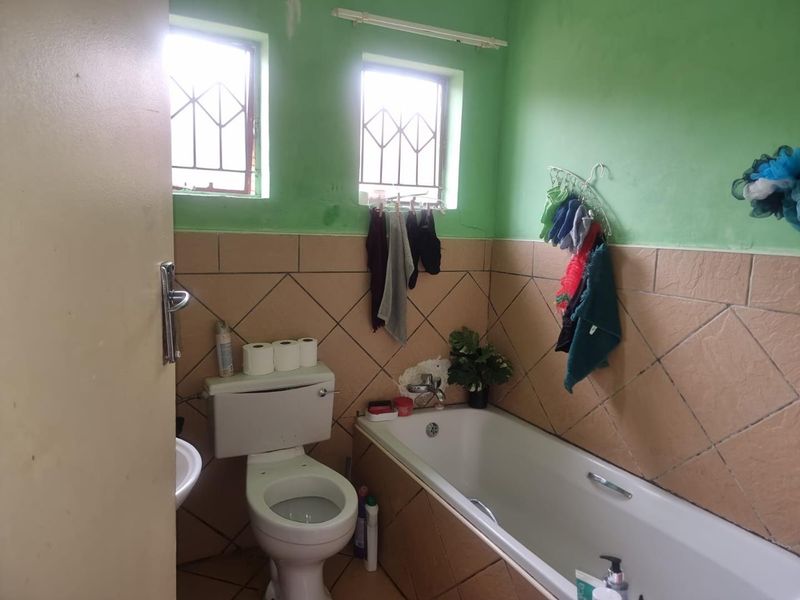 A functional bathroom featuring a bathtub, toilet, and basin with tiled walls and security bars on the windows.