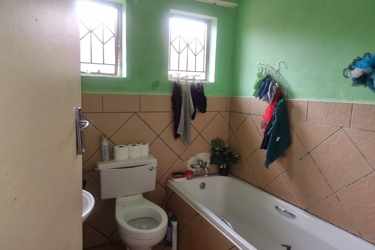 A functional bathroom featuring a bathtub, toilet, and basin with tiled walls and security bars on the windows.