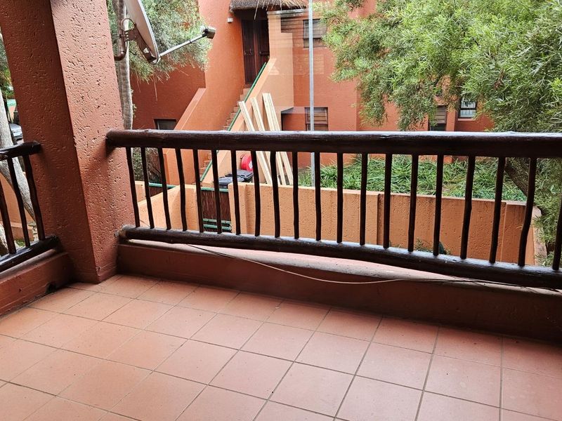 A covered balcony featuring tiled flooring and a wooden balustrade, overlooking the complex grounds.