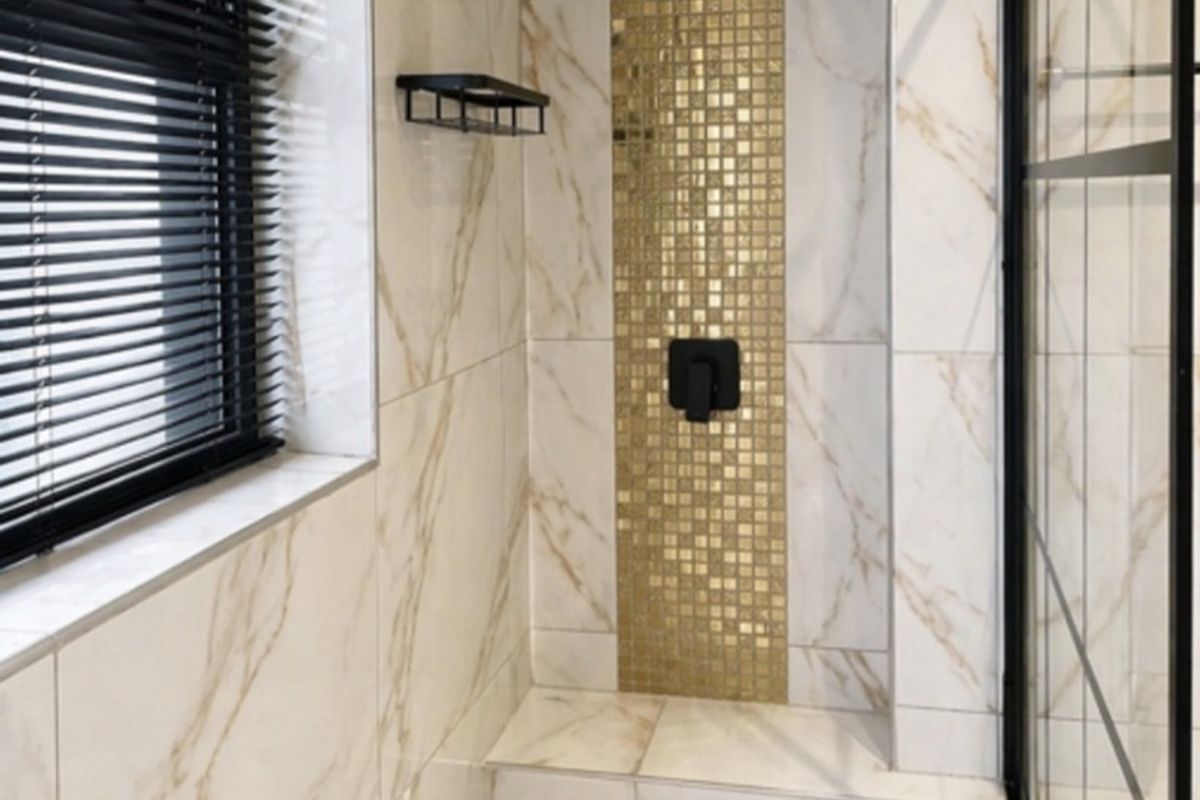 Modern walk-in shower featuring marble-look wall tiles, a gold mosaic feature strip, built-in bench, and contemporary black fixtures.