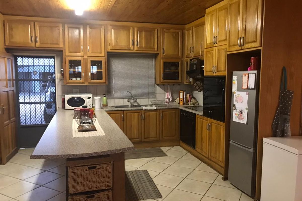 A functional kitchen featuring timber cabinetry, a central island with stone-look countertop, tiled flooring, and a built-in oven with extractor fan.
