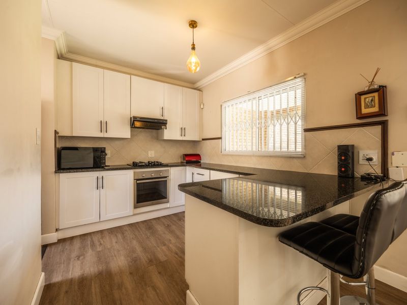 A well-maintained kitchen featuring white cabinetry, granite countertops, a breakfast bar, and built-in appliances including an oven and gas hob.