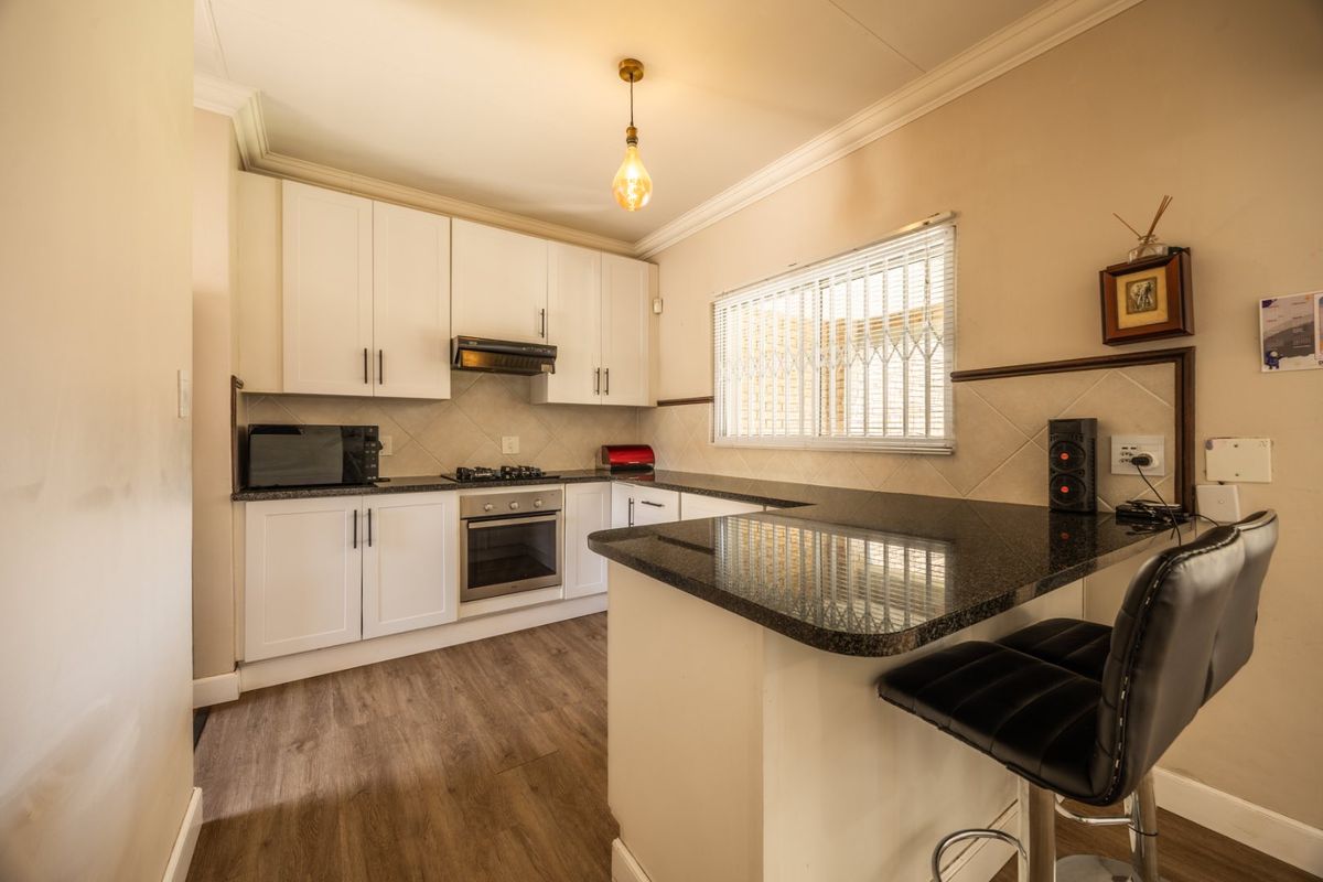 A well-maintained kitchen featuring white cabinetry, granite countertops, a breakfast bar, and built-in appliances including an oven and gas hob.