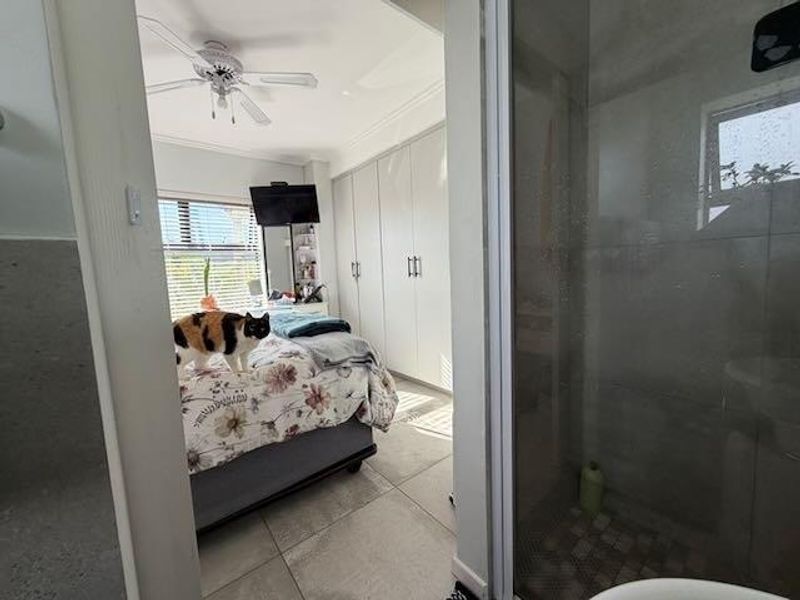 A bedroom featuring built-in cupboards, tiled flooring, and a ceiling fan, with an adjacent shower enclosure visible in the foreground.
