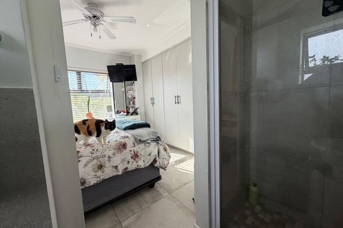 A bedroom featuring built-in cupboards, tiled flooring, and a ceiling fan, with an adjacent shower enclosure visible in the foreground.