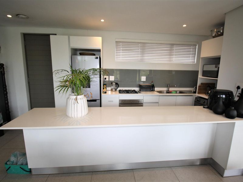 Modern kitchen featuring a large central island, sleek cabinetry, glass splashback, built-in gas hob, and oven with integrated sink and recessed lighting.