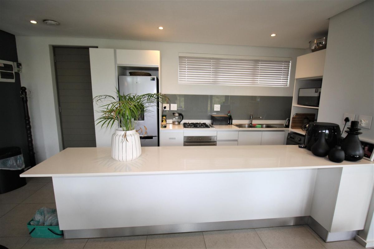 Modern kitchen featuring a large central island, sleek cabinetry, glass splashback, built-in gas hob, and oven with integrated sink and recessed lighting.