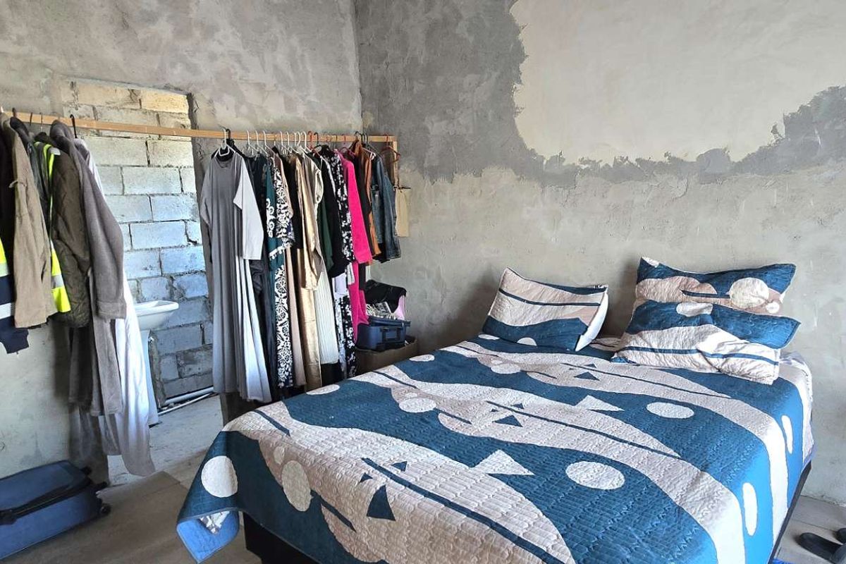 A bedroom featuring unfinished concrete walls and laminate flooring, currently requiring plastering and finishing to complete the interior space.