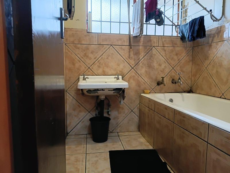 A dated bathroom featuring a built-in bathtub and a wall-mounted basin with visible wear on the basin finish and tiled surfaces.