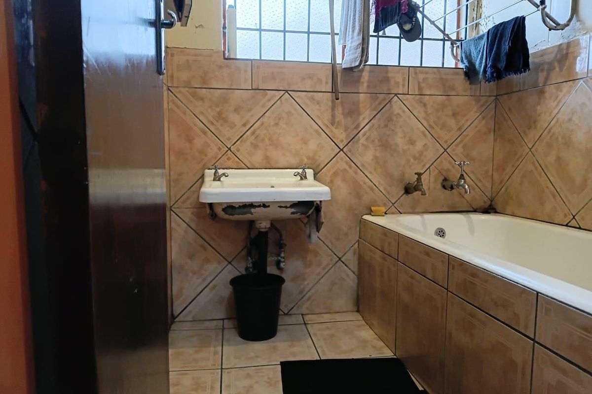 A dated bathroom featuring a built-in bathtub and a wall-mounted basin with visible wear on the basin finish and tiled surfaces.