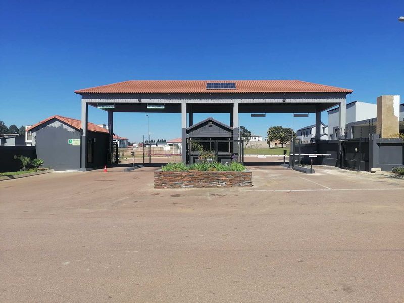 A well-maintained residential estate entrance featuring a security gatehouse, boom gates, and solar-powered infrastructure.