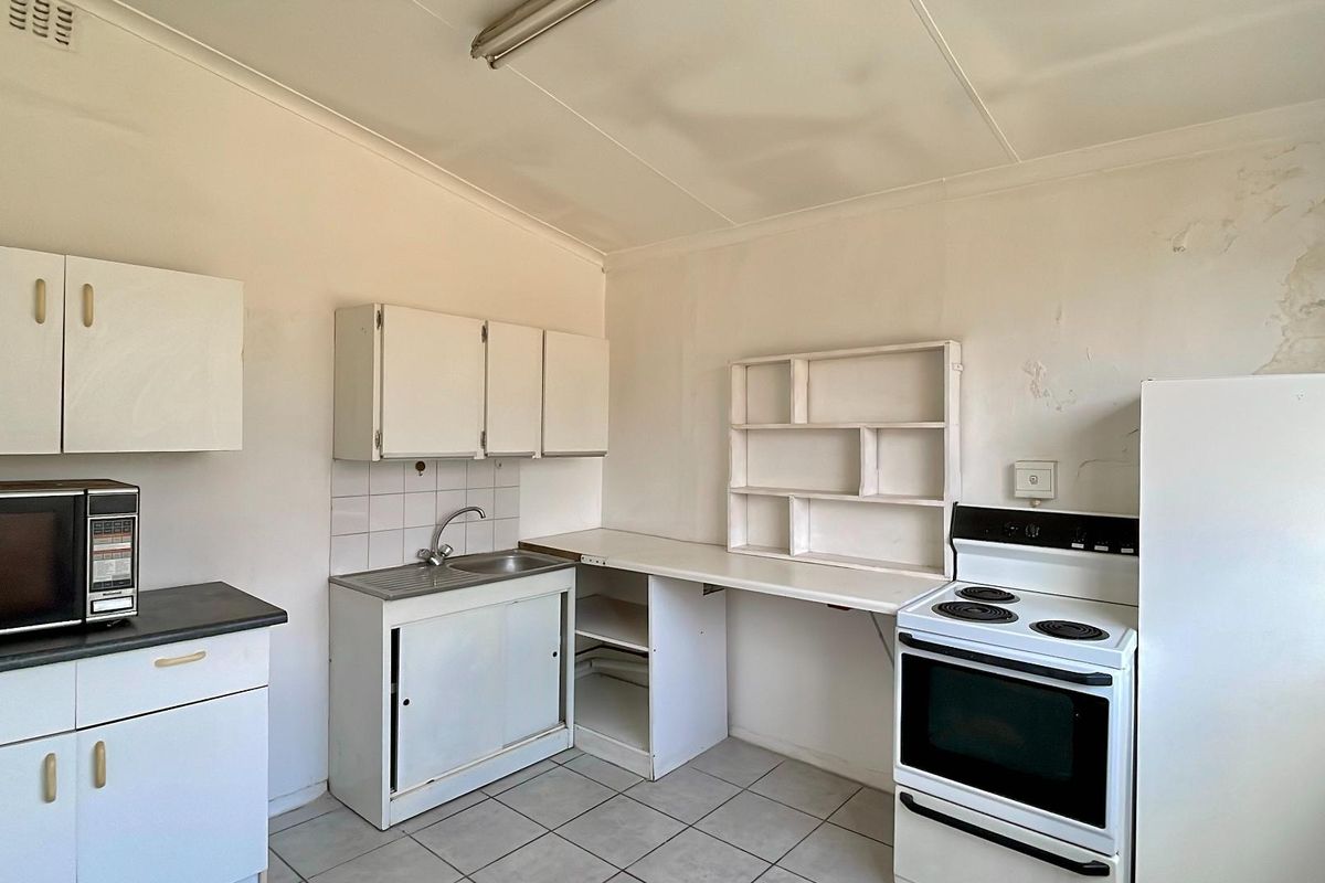 A dated kitchen featuring basic white cabinetry, a stainless steel sink, and a freestanding electric stove, requiring cosmetic updates and repairs to wall finishes.