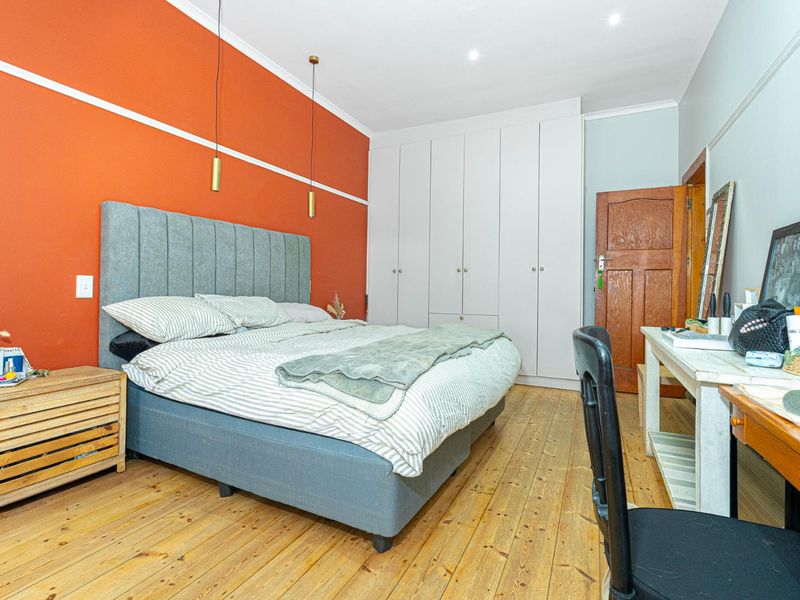 A well-lit bedroom featuring polished timber flooring, built-in floor-to-ceiling cupboards, and a bold accent wall with modern pendant lighting.