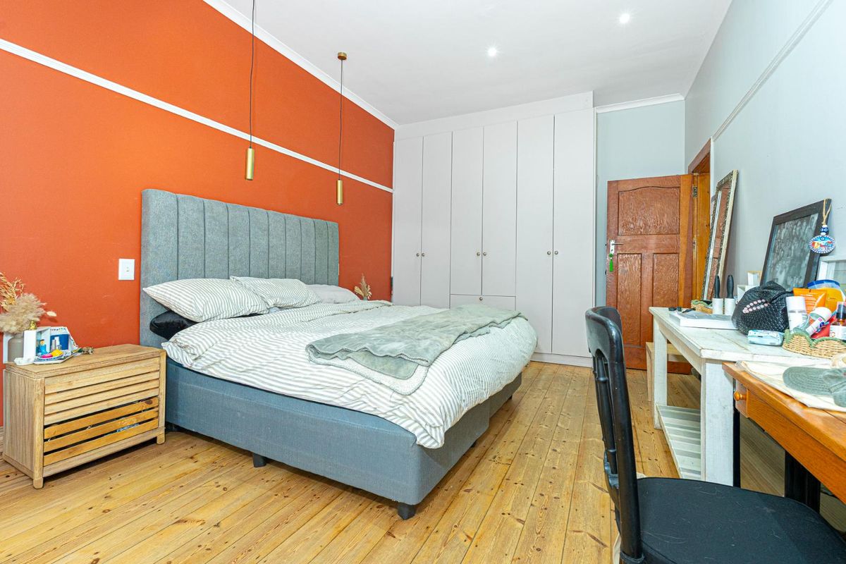 A well-lit bedroom featuring polished timber flooring, built-in floor-to-ceiling cupboards, and a bold accent wall with modern pendant lighting.