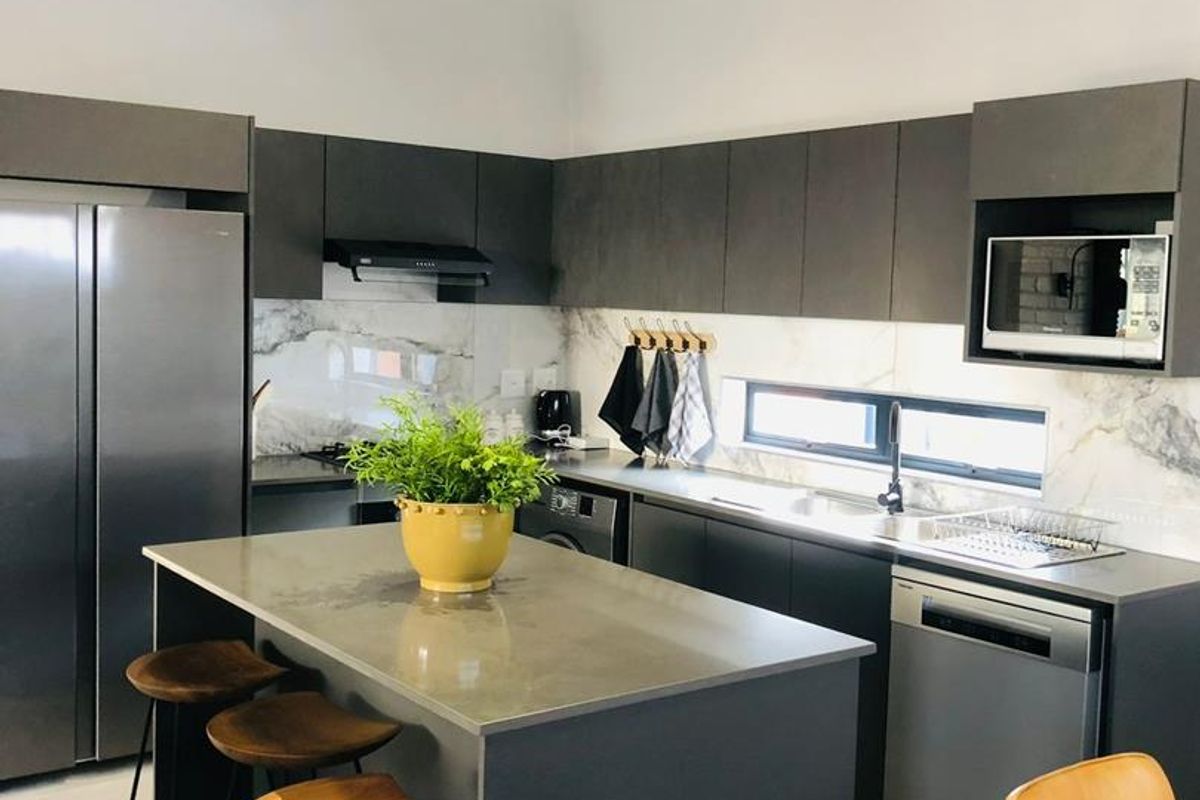 Modern kitchen featuring dark cabinetry, stone countertops, marble-look backsplash, central island, and vaulted ceilings with exposed beams.