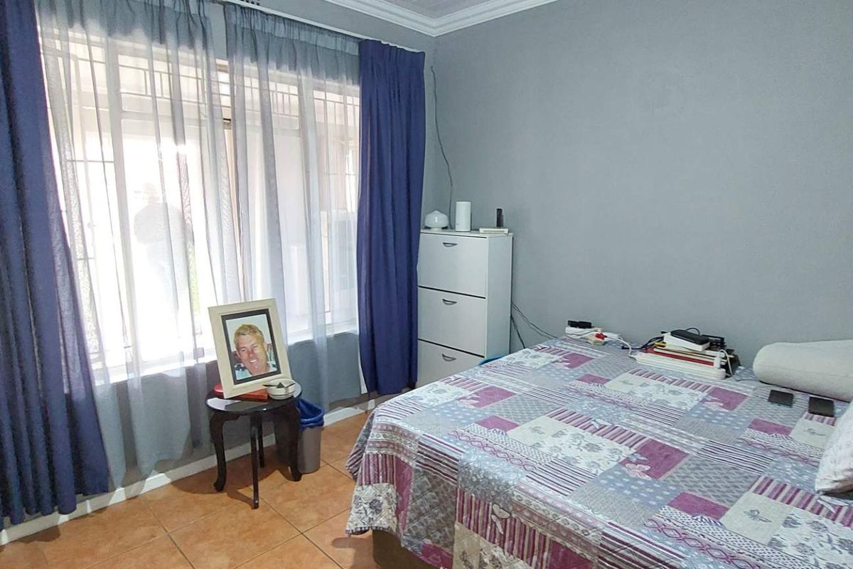 A bedroom featuring tiled flooring, crown molding, and large windows with security bars, providing natural light.