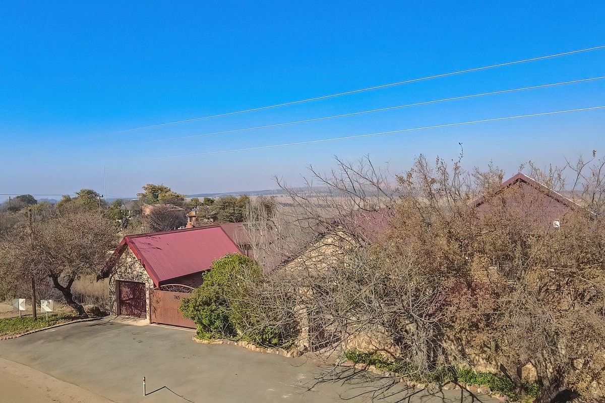 An elevated aerial view of a residential property featuring stone-clad exterior walls, a metal roof, and a paved driveway.
