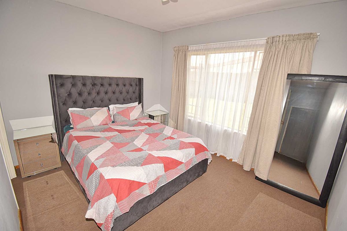 A standard bedroom featuring carpeted flooring and a large window with installed curtain tracks, providing natural light to the space.