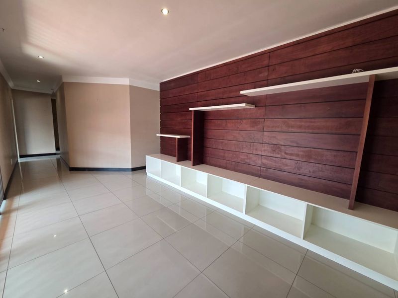 A bright, empty office space featuring polished tile flooring, recessed lighting, and a modern wood-paneled feature wall with integrated built-in shelving.