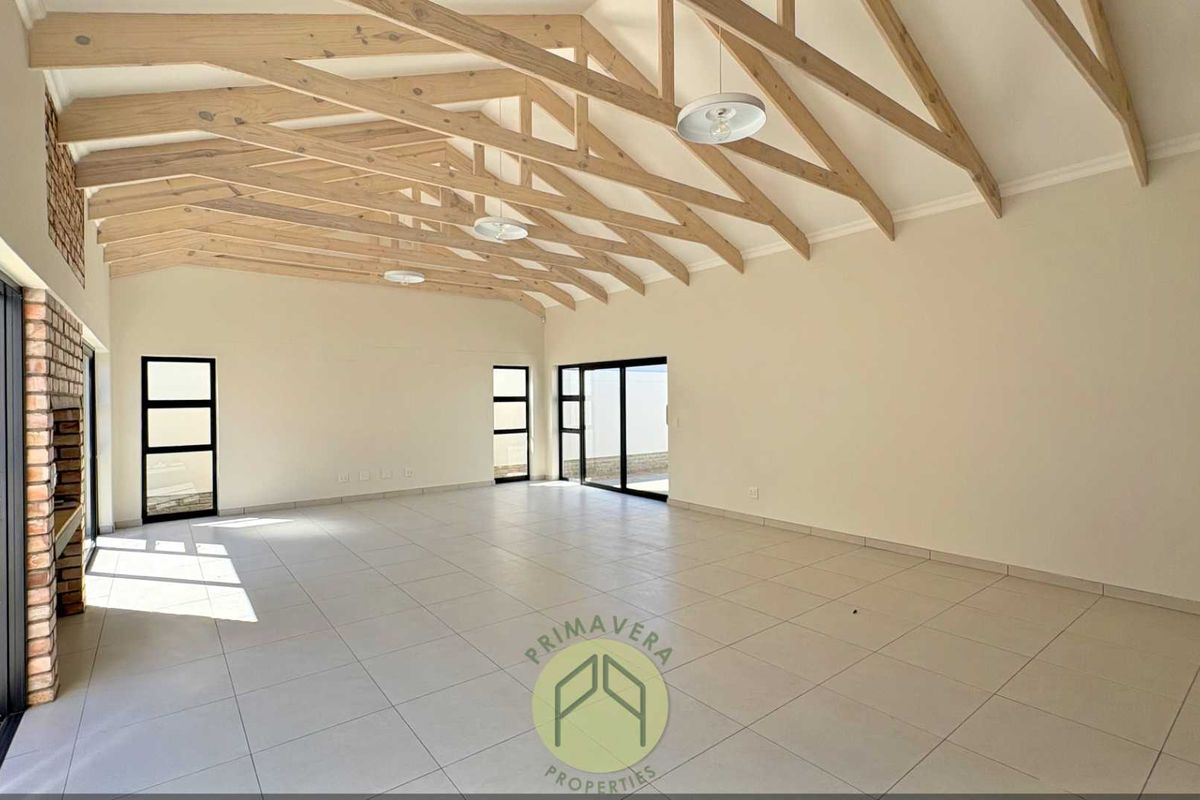 Spacious open-plan living area featuring high vaulted ceilings with exposed timber trusses, tiled floors, and large sliding doors leading to the exterior.