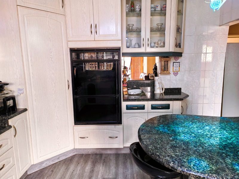 A functional kitchen featuring built-in oven, granite countertops, and light-toned cabinetry with glass-front display units.