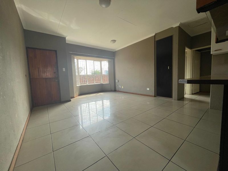 Spacious, empty living area featuring large tiled flooring, a bay window with security bars, and neutral wall tones.