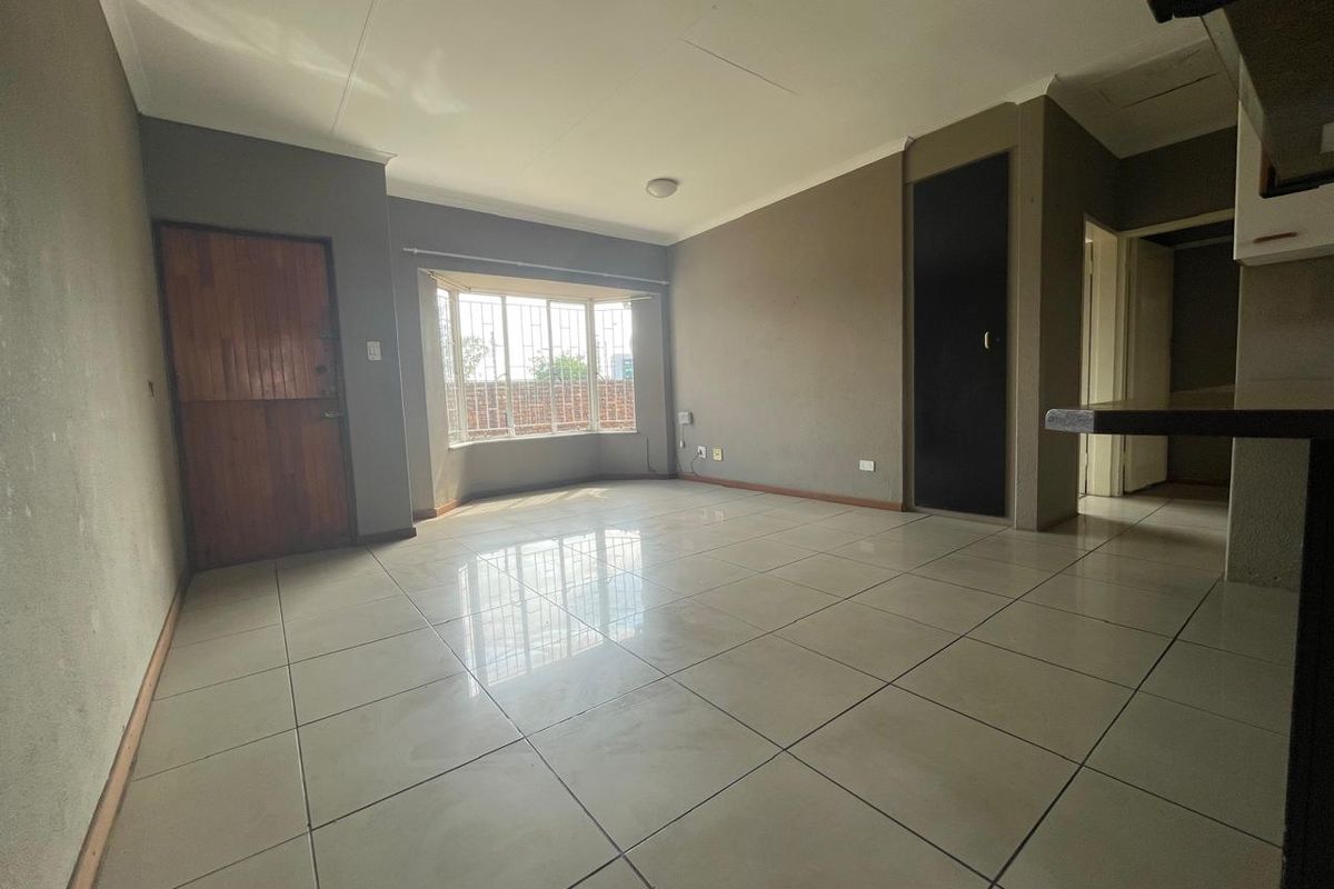 Spacious, empty living area featuring large tiled flooring, a bay window with security bars, and neutral wall tones.