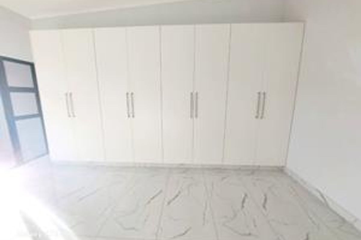 A bright, empty bedroom featuring modern white built-in cupboards and large-format marble-look floor tiles.
