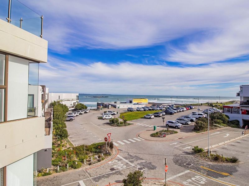 Elevated coastal view overlooking a parking area, surrounding commercial buildings, and the ocean horizon.