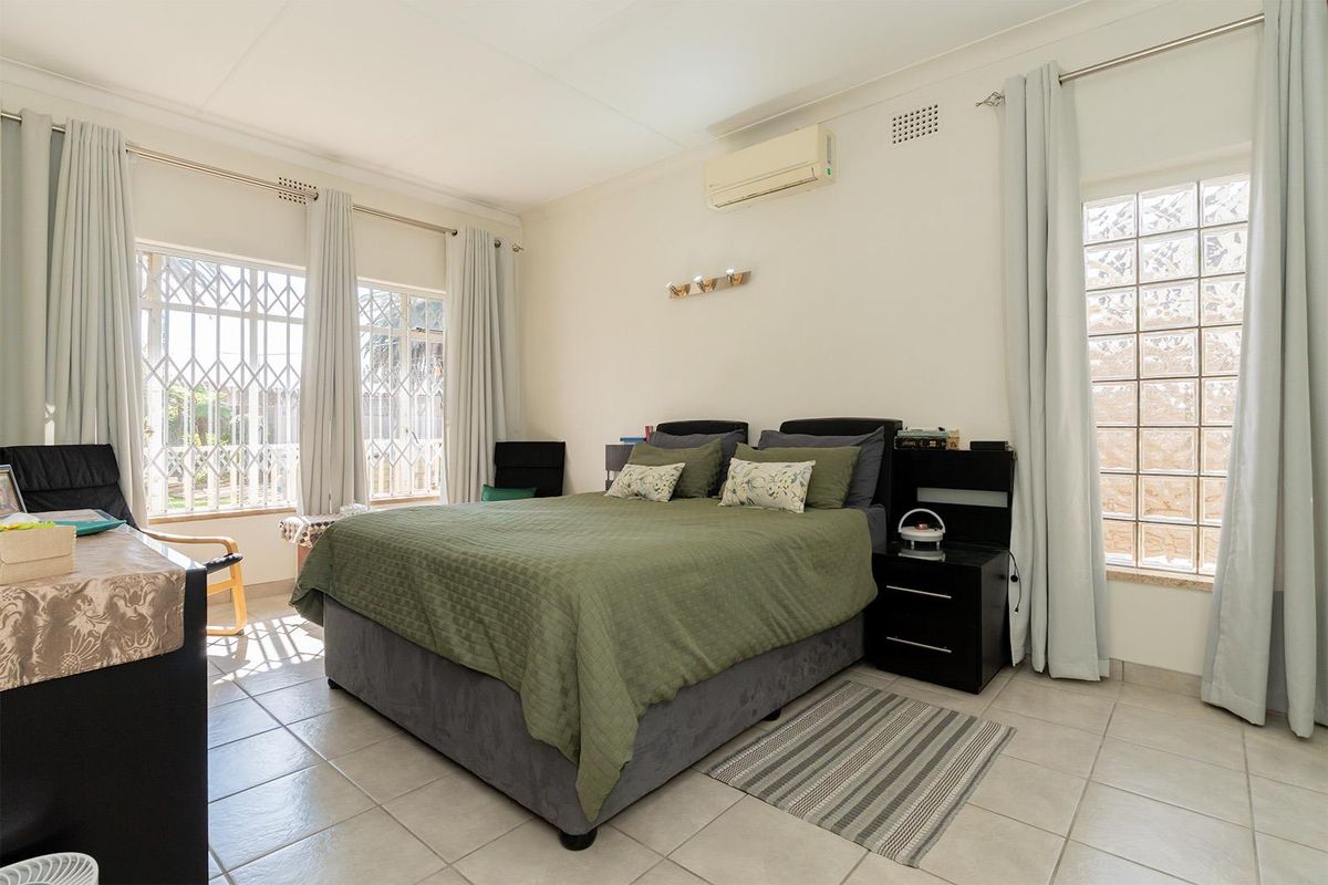 Spacious bedroom featuring tiled flooring, wall-mounted air conditioning unit, and large windows with security bars, providing ample natural light.