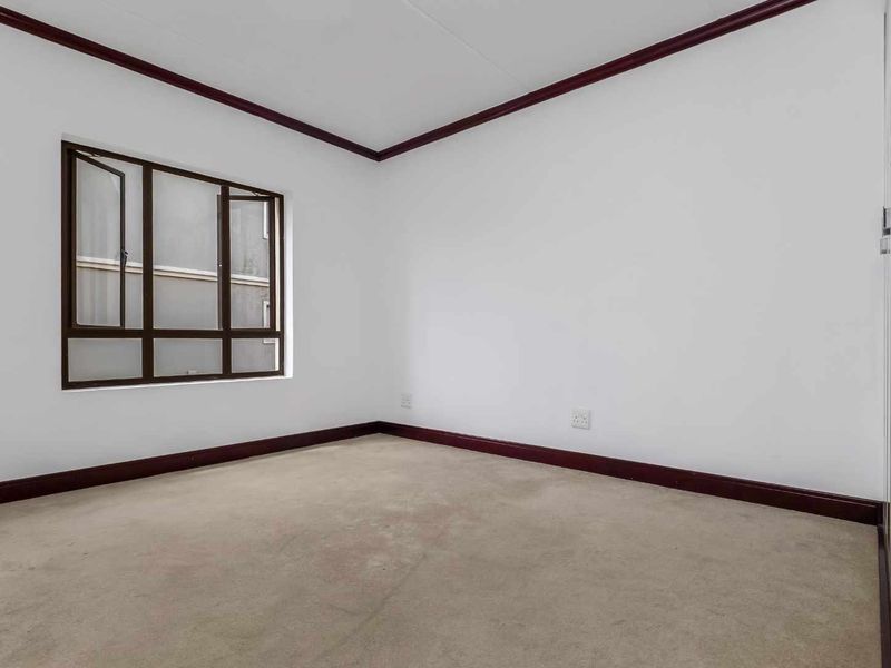 An empty bedroom featuring neutral walls, dark trim accents, a built-in wardrobe, and carpeted flooring.