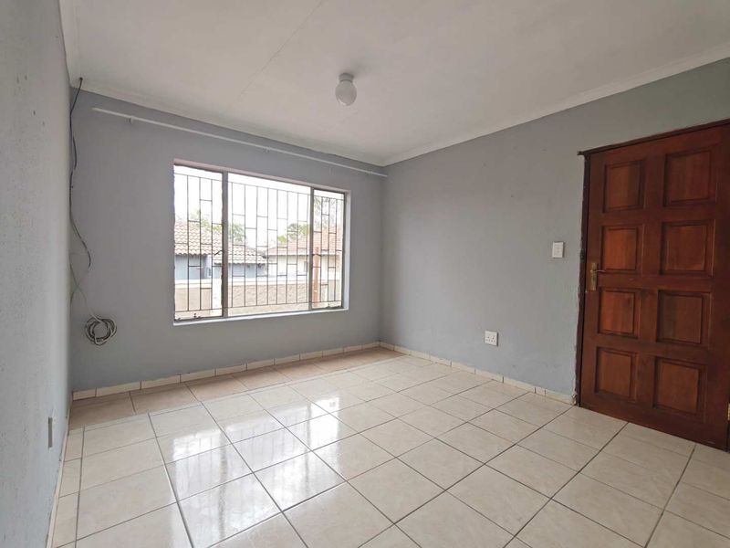 A vacant bedroom featuring tiled flooring, a wooden door, and a window fitted with security bars.
