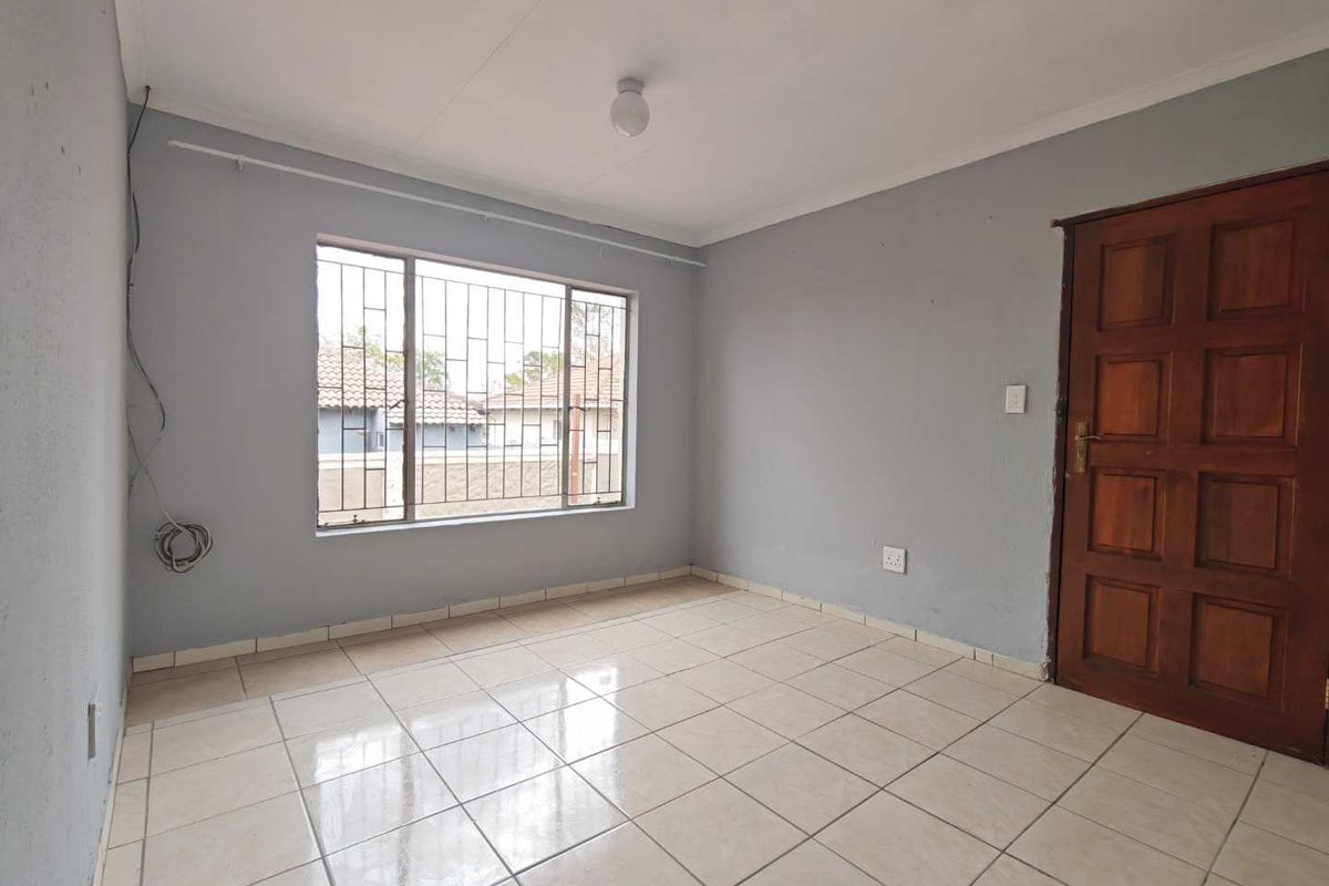 A vacant bedroom featuring tiled flooring, a wooden door, and a window fitted with security bars.