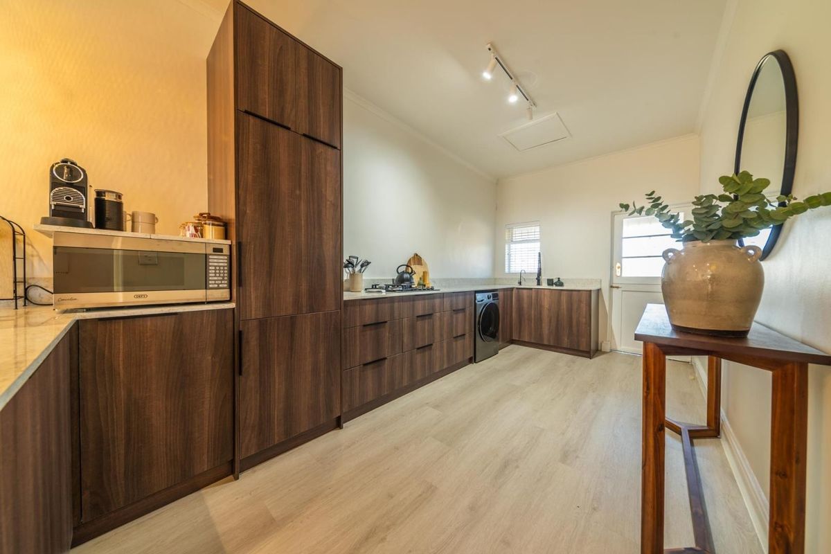 Modern kitchen featuring dark wood cabinetry, light stone countertops, integrated appliances, and light wood-look flooring with direct access to an exterior door.