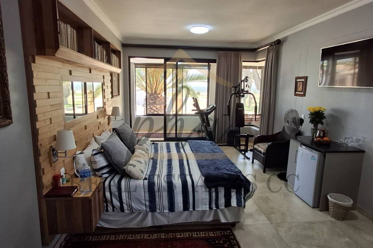 Spacious bedroom featuring built-in wooden headboard with integrated shelving, tiled flooring, and large sliding glass doors providing natural light and outdoor access.