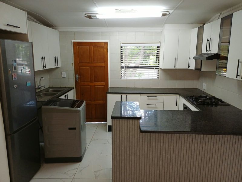 Functional kitchen featuring white cabinetry, dark granite countertops, gas hob, extractor fan, and tiled flooring with a convenient breakfast counter.